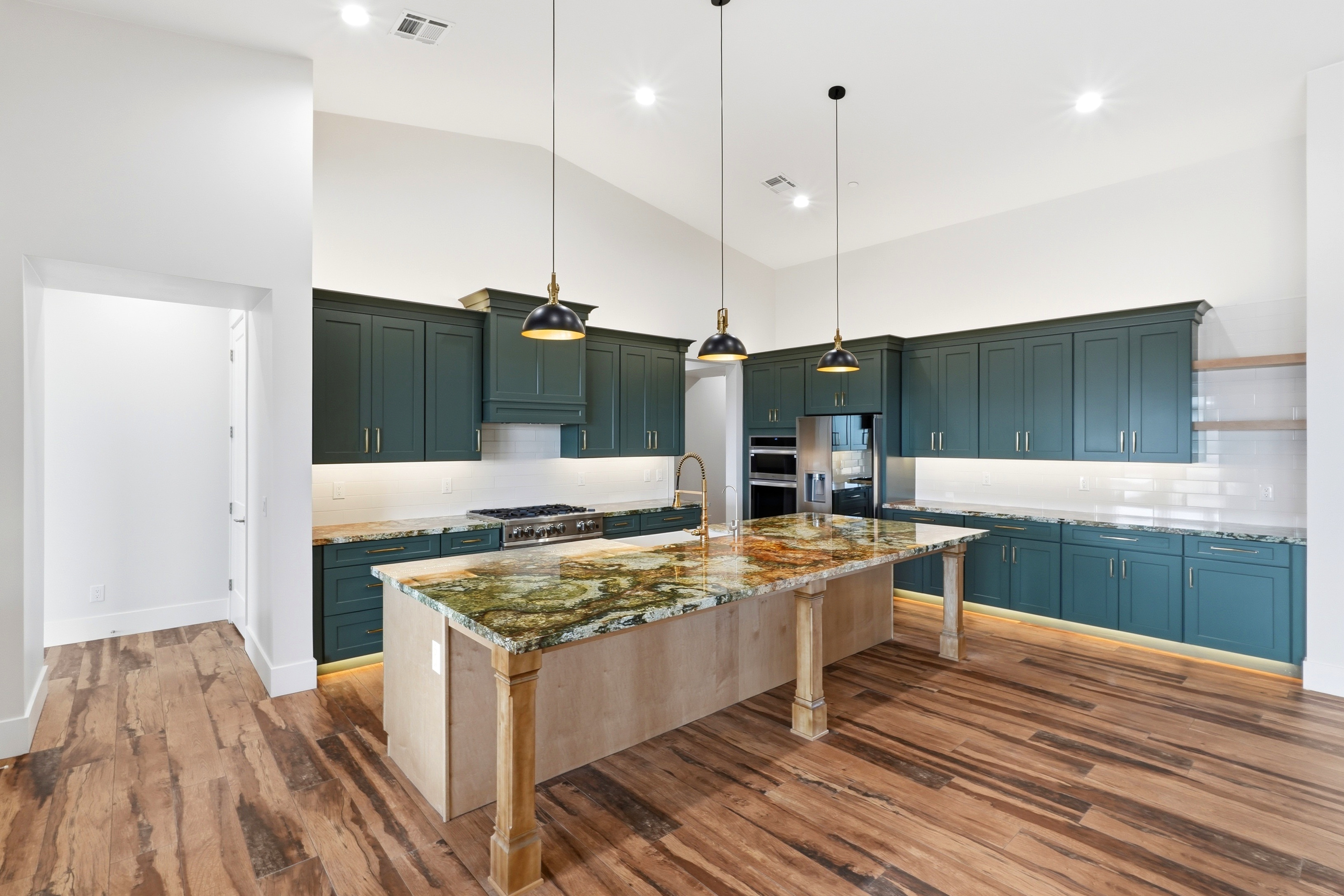 Custom kitchen by Jematell Homes with deep green cabinetry, a natural stone waterfall island, and vaulted ceilings